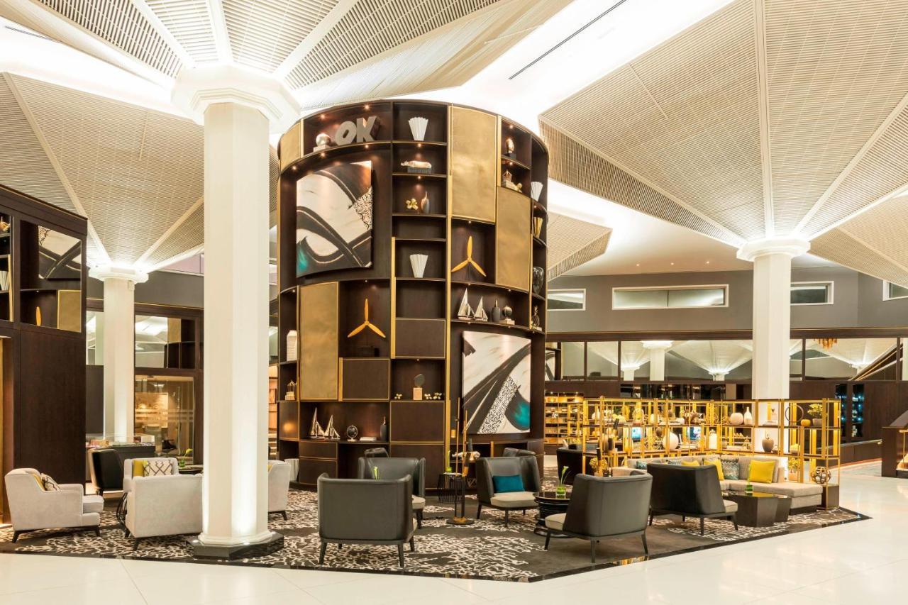 Le Meridien Dubai Hotel & Conference Centre Exterior foto The photo depicts a modern lounge or waiting area, characterized by a sleek and contemporary design. A prominent feature is a tall, circular shelving unit that displays various decorative items and art pieces, incorporating elements of gold and abstr