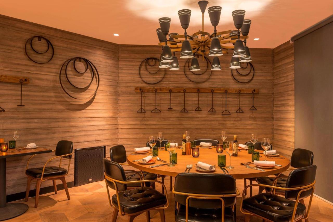 Le Meridien Dubai Hotel & Conference Centre Exterior foto The photo shows a modern dining room with a circular wooden table surrounded by stylish black chairs. The walls are adorned with a textured design and feature some circular decorations, possibly made of metal or wood. Above the table, there is a uniq