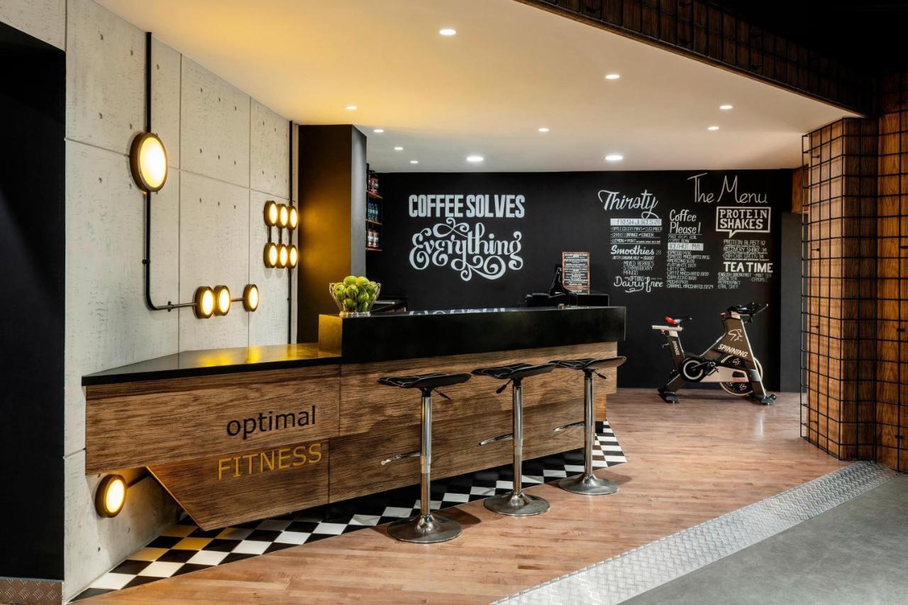 Le Meridien Dubai Hotel & Conference Centre Exterior foto The photo showcases a modern fitness reception area. A sleek wooden reception desk with the words "optimal FITNESS" is positioned prominently. Behind the desk, a black wall features motivational phrases and chalkboard-style text, including "COFFEE SO