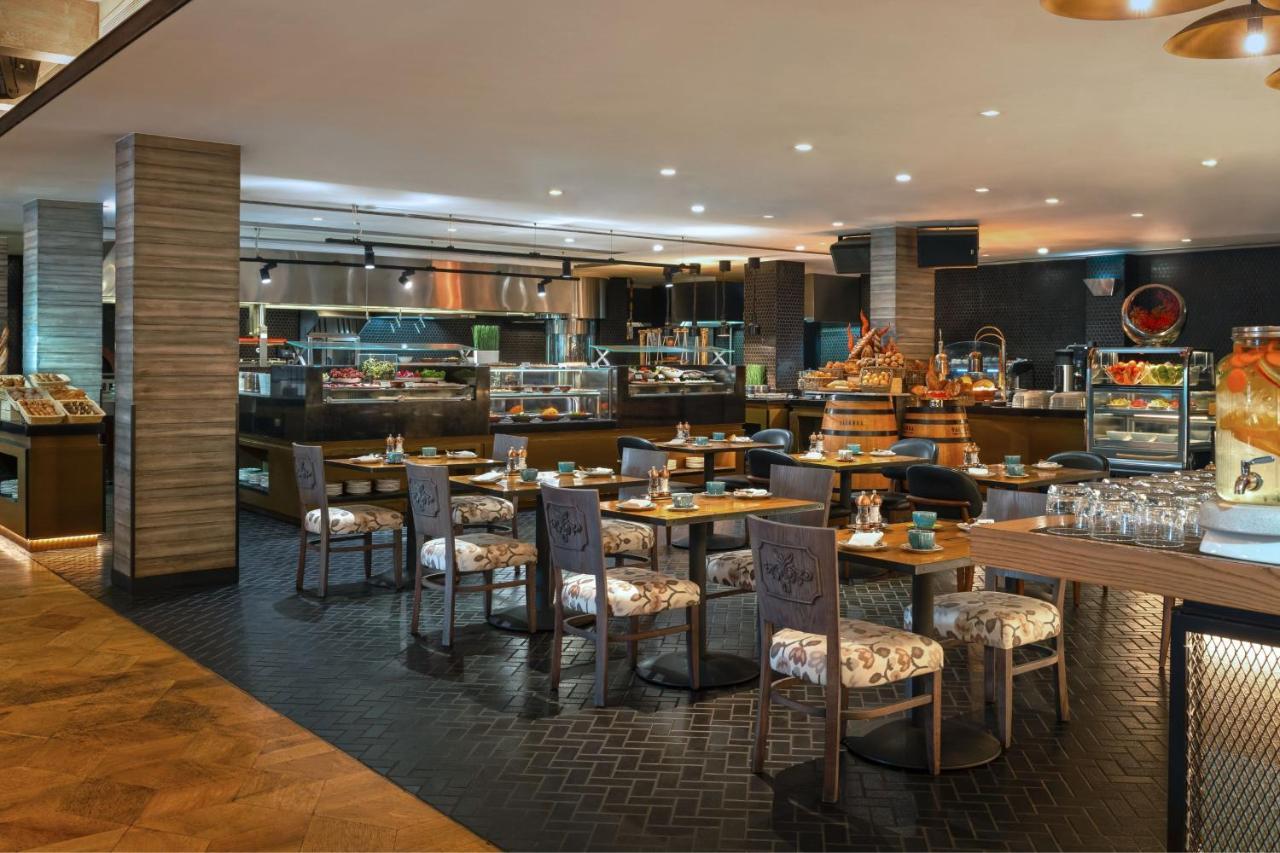 Le Meridien Dubai Hotel & Conference Centre Exterior foto The photo depicts a modern restaurant interior. It features a spacious dining area with several tables and chairs arranged thoughtfully. The tables have floral-patterned upholstery, creating a warm and inviting atmosphere. 

In the background, there 