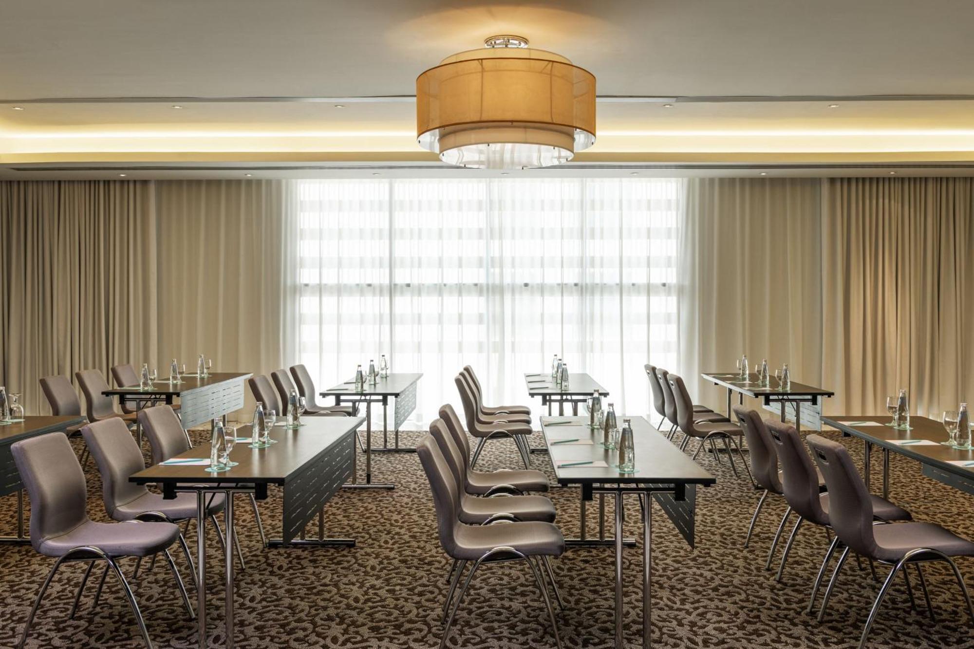 Le Meridien Dubai Hotel & Conference Centre Exterior foto The photo shows a conference room set up for meetings or presentations. There are several rows of tables with chairs arranged in a classroom style. Each table has a water bottle, suggesting that it is prepared for participants. The room is well-lit, 